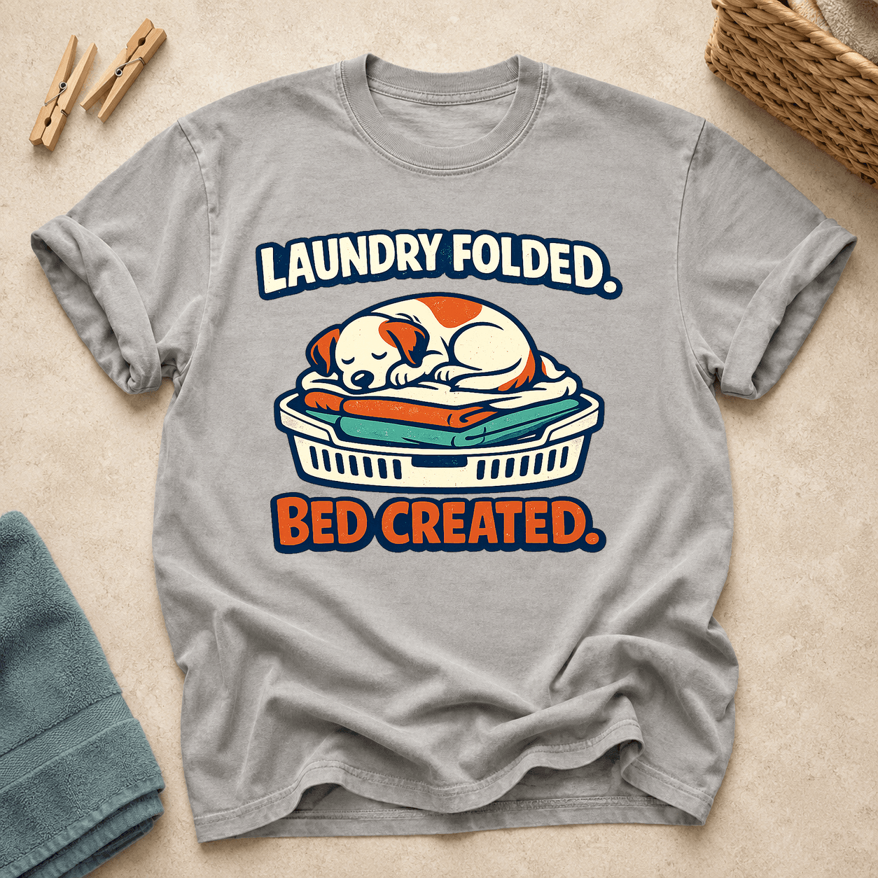 Grey Comfort Colors T-shirt printed with Laundry Folded. Bed Created. and a sleeping dog curled on a basket of folded clothes.