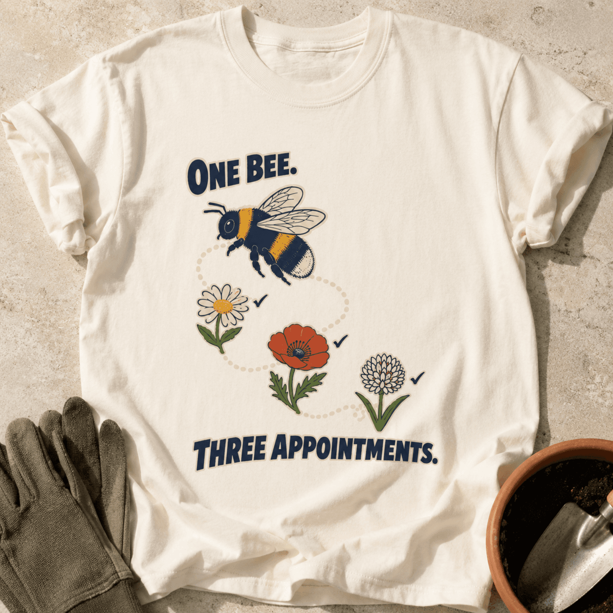 Ivory Comfort Colors T-shirt printed with One Bee. Three Appointments., styled with rolled sleeves, gardening gloves, a terracotta pot and hand trowel.